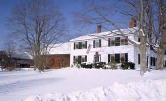 a large white house with a red brick chimney is surrounded by snow and trees at Colby Hill Inn