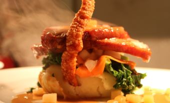 a plate of food , consisting of a burger topped with meat and vegetables , sitting on a dining table at King William Inn