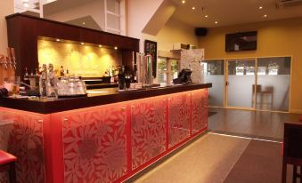 a bar with red and gold cabinets , a counter , and various bottles on display behind it at Garden Hotel