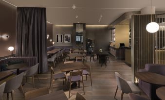 a modern restaurant with wooden tables and chairs , a bar area , and black curtains , lit by ceiling lights at Adina Apartment Hotel Nuremberg