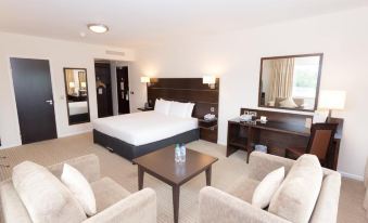 a large bed with a white comforter is in the middle of a room with beige chairs and a table at DoubleTree by Hilton London Heathrow Airport