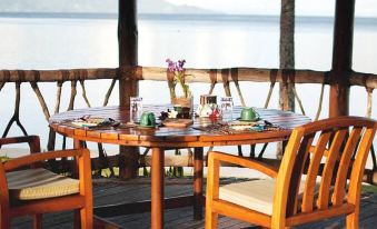 a wooden table set with various items and glasses , surrounded by chairs on a balcony overlooking water at The Wakaya Club & Spa
