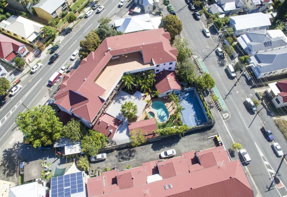 an aerial view of a large , red - roofed building with a swimming pool and surrounding greenery at Brisbane Backpackers Resort