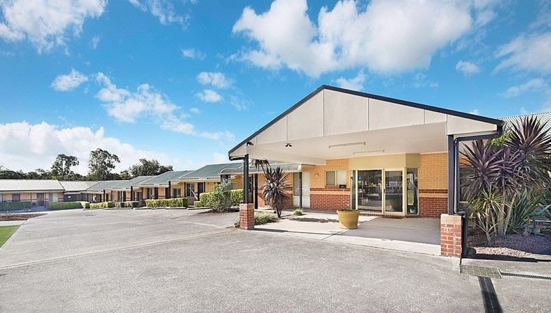 an exterior view of a motel with a parking lot in front of it , surrounded by trees and other buildings at Catalina Motel Lake Macquarie