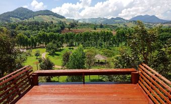 a wooden deck overlooking a lush green landscape , with mountains in the background and a cloudy sky overhead at Phufatara Resort