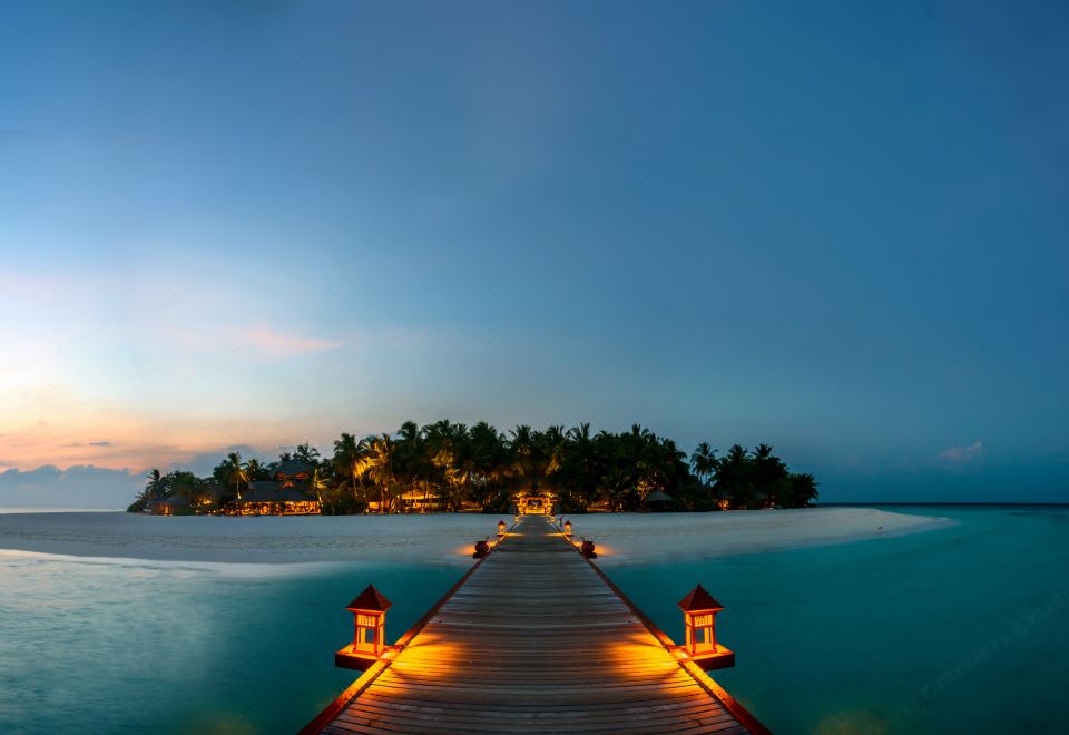 a wooden pier with lanterns leading to an island in the middle of a blue ocean at Banyan Tree Vabbinfaru