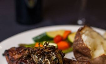 a plate of steak and mashed potatoes with a side of vegetables and a glass of wine at Three Rivers Casino Resort