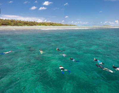 a group of people in snorkeling gear are swimming in the clear blue water near a sandy beach at Vilamendhoo Island Resort & Spa