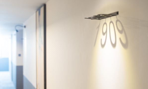 "a modern , white - walled hallway with a hanging light and a sign reading "" 9 0 9 "" on the wall" at Z Hotel Johor Bahru