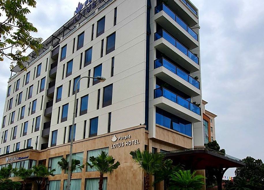 a tall , modern building with blue and white accents , surrounded by trees and a road at Purple Lotus Hotel