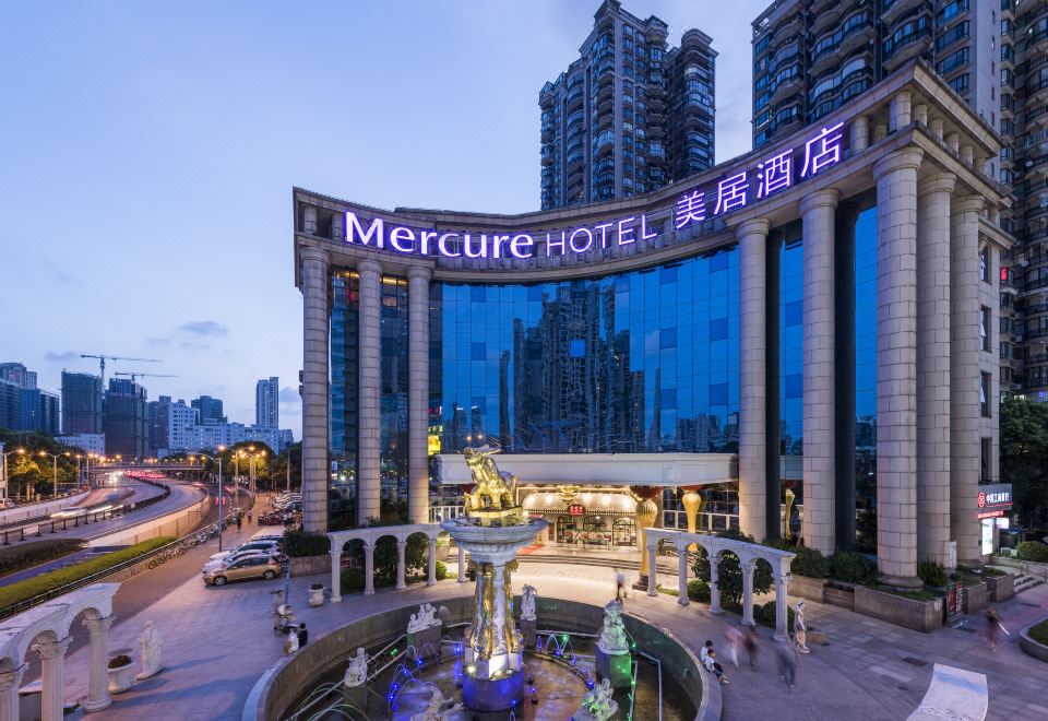 "There is a large building with an illuminated ""hotel"" sign on top, offering a view of the exterior at night" at Mercure Shanghai Yu Garden On the Bund