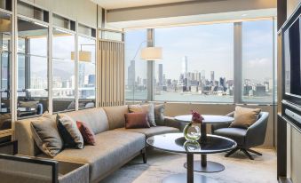 a living room with large windows and a view outside, with a couch facing the windows at Hyatt Centric Victoria Harbour Hong Kong