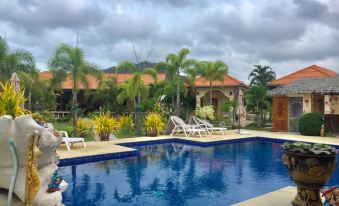 a large , rectangular pool is surrounded by lounge chairs and a house with red tile roof at Stella Resort