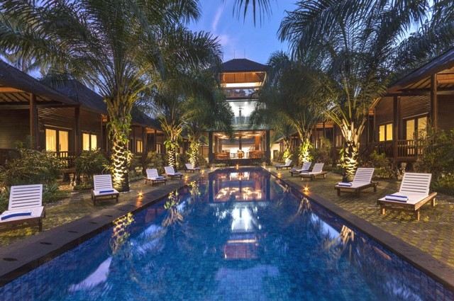 a large swimming pool surrounded by palm trees , with lounge chairs and umbrellas placed around it at Coconut Boutique Resort