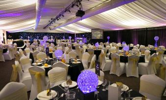 a large event hall with white tables and chairs , purple lights on the ceiling , and blue balls at Tewinbury