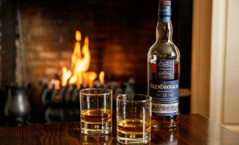 a bottle of glendronach whisky and two glasses are placed on a table in front of a fireplace at Fife Arms Hotel