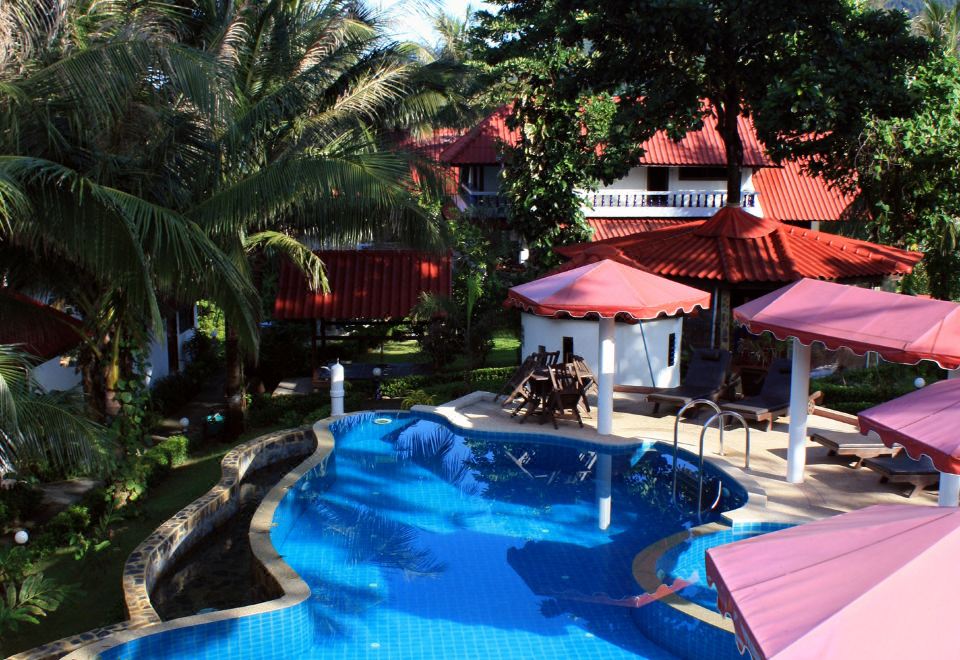 a large swimming pool with a water slide is surrounded by red umbrellas and palm trees at Top Resort