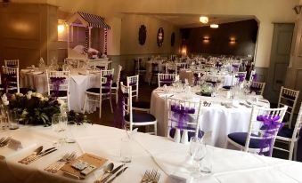 a lavishly decorated banquet hall with numerous dining tables covered in white tablecloths and chairs arranged for a wedding reception at The Old Lodge