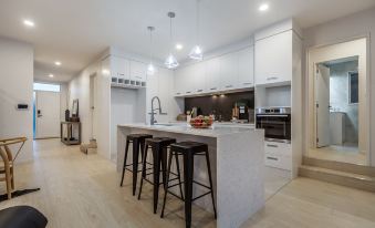a modern kitchen with white cabinets , a large island with a bar stools , and pendant lights hanging from the ceiling at Flat Bush Holiday Accomodation
