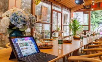 In the middle of the room, there is a wooden table with chairs and a laptop on it, positioned next to large windows at Zhouzhuang Latte Play Stone Mulan Hotel