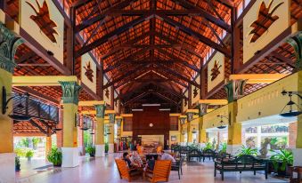 a large , open lobby with wooden beams and a high ceiling , where people are sitting at tables and enjoying their time at Pandanus Resort