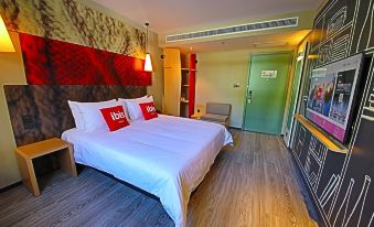 a large bed with white sheets and red pillows is in a room with wooden floors at Ibis Hotel