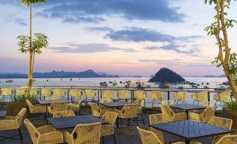 a restaurant patio with yellow chairs and tables , overlooking a body of water at sunset at Meruorah Komodo Labuan Bajo