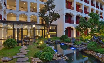 a modern building with multiple floors , a garden area , and a waterfall , lit up at night at Senna Hue Hotel