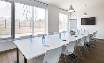 a long table with white chairs and blue water bottles is set up in a conference room at B&B Hotel Barcelona Viladecans