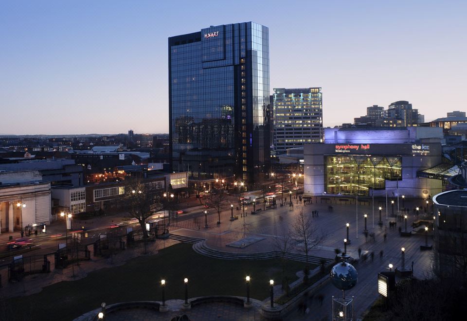 a city skyline at night , with the illuminated hilton hotel in the foreground and other buildings surrounding a park area at Hyatt Regency Birmingham