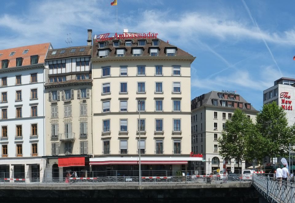 a large white building with a red sign on the front is situated next to a body of water at The Ambassador