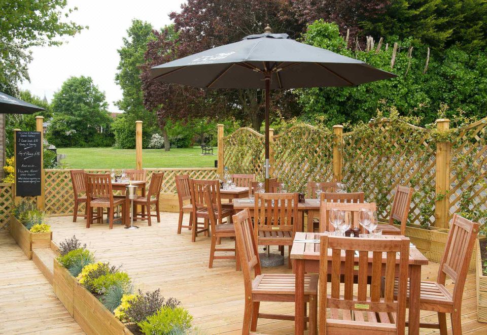 an outdoor dining area with wooden tables and chairs , as well as an umbrella providing shade at The Lamb at Angmering