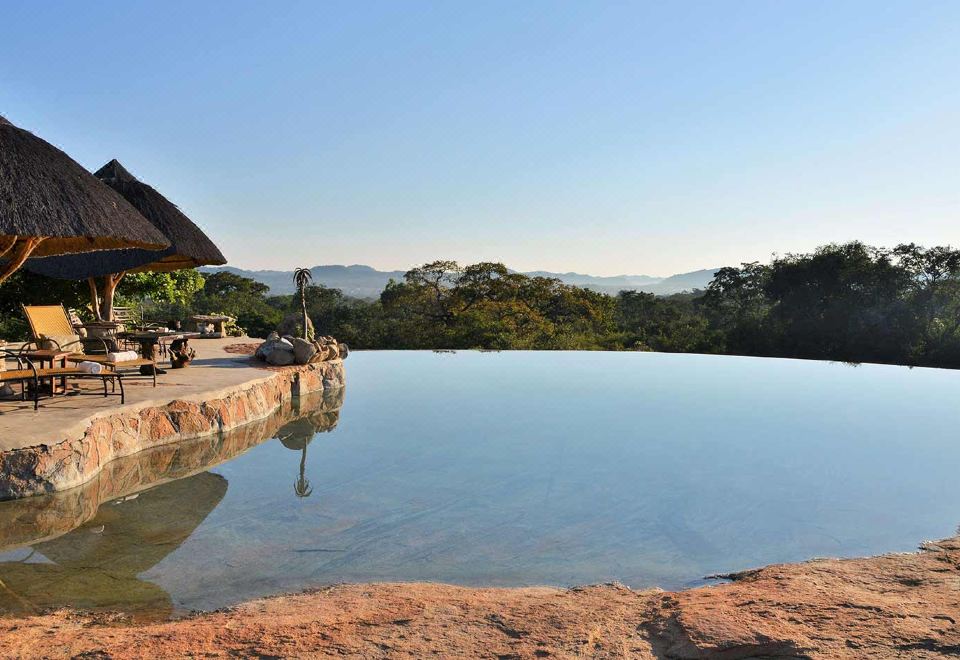 a large outdoor pool surrounded by lush greenery , with a gazebo in the background at Amalinda Lodge