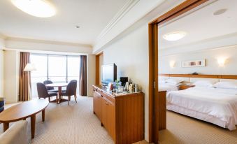 a hotel room with a bed , desk , and tv , as well as a view of the ocean through a window at Sheraton Grande Tokyo Bay Hotel