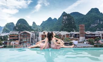 A woman is seen in the pool, her reflection visible in another swimming area, while other people sit around at Zhenmei Resort Chain Hotel(Yangshuo West Street AiYuan Store)