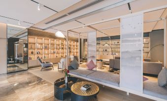 The room is filled with bookshelves, and it also has large windows, chairs, and tables in the middle at Atour Hotel (Yiwu International Trade City)