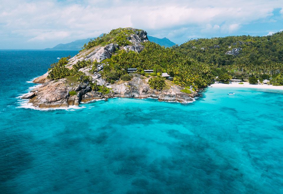 a picturesque view of a small island surrounded by clear blue water , with a beach visible in the distance at North Island, a Luxury Collection Resort, Seychelles