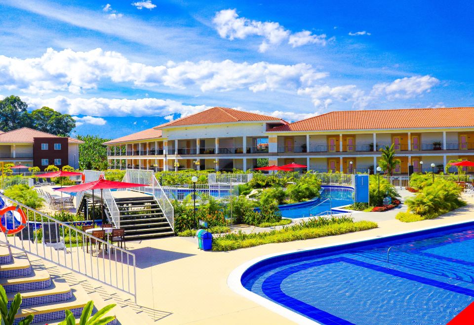 a large resort with multiple buildings , swimming pools , and lush greenery under a blue sky at Hotel Campestre las Camelias