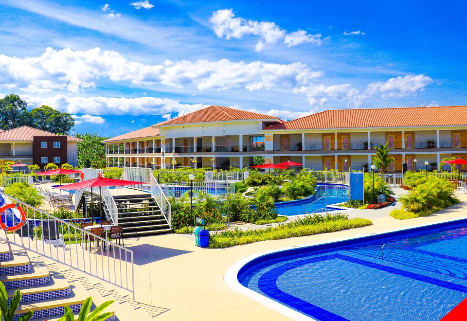 a large , modern hotel with a swimming pool and lush greenery in the foreground , set against a blue sky at Hotel Campestre las Camelias