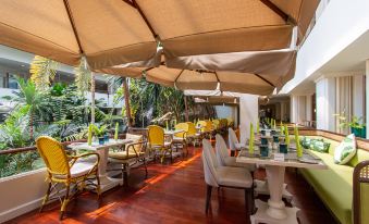 a restaurant with a wooden floor , white tables and chairs , and large umbrellas providing shade at Dusit Thani Pattaya