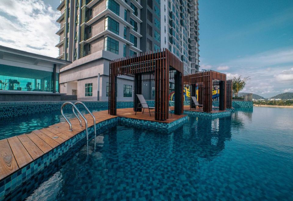 a swimming pool with a wooden deck and lounge chairs in front of a tall building at Swiss-Belhotel Kuantan