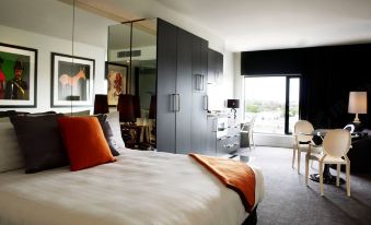 a large bed with white sheets and an orange blanket is in a room with gray walls at The Cullen Melbourne - Art Series