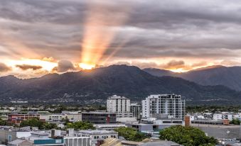 a cityscape with a mountain in the background and a sunbeam shining through clouds on top of it at Pacific Hotel Cairns