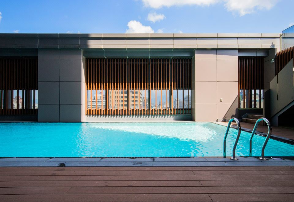 There is an outdoor deck next to a swimming pool with chairs and tables at Caesar Metro Taipei