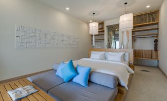 a modern bedroom with a large bed , white bedding , and blue pillows , along with a wooden floor and pendant lights at Que Toi Village Resort Phu Yen