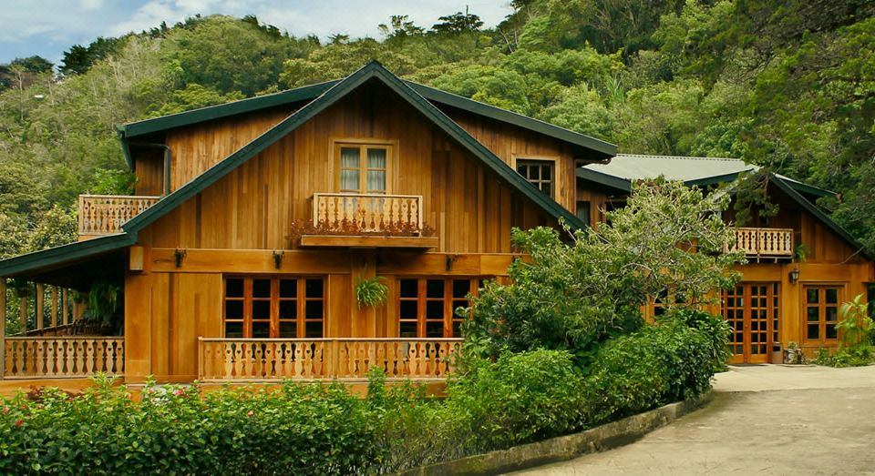 a wooden house surrounded by trees and bushes , with a balcony on the second floor at Hotel Belmar