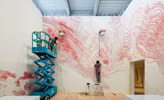 two people are working together on a red and white wall , with some lifting equipment nearby at Hotel Anteroom Naha