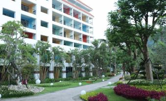 a tall white building with balconies is surrounded by trees and bushes , and has a pathway leading to it at Hotel Cham Cham