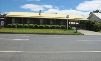 a yellow building with a green lawn in front of it , surrounded by grass and trees at Country Road Motel St Arnaud