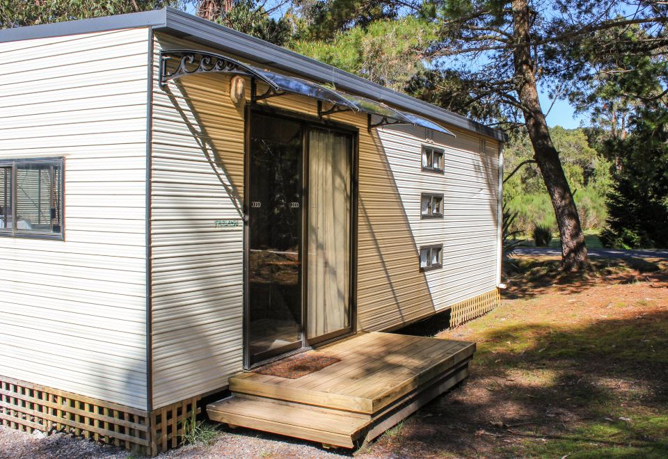 a small white wooden house with a porch and a door , situated in a wooded area at Zeehan Bush Camp